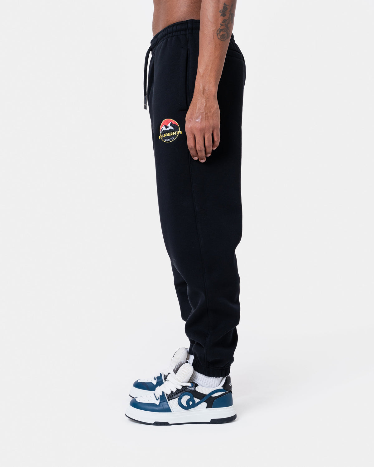 ALASKA BADGE BLACK JOGGER side view showing pockets and logo detail on a model wearing sneakers.
